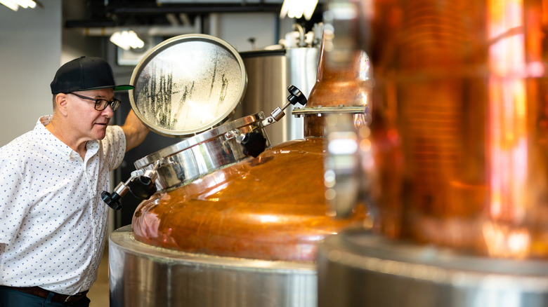 A distiller looks into a copper still.