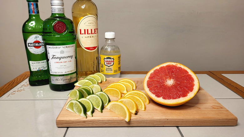 A bottle of Tanqueray next to a wooden cutting board with slices of citrus fruit: lemons, limes, and grapefruit.