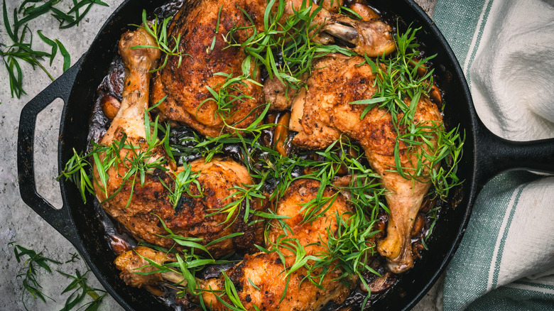Sprigs of fresh tarragon scattered over baked chicken legs in skillet