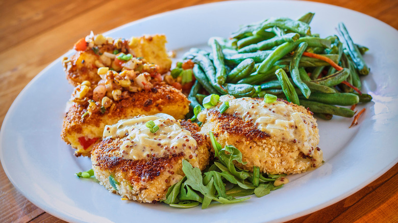 Crab cakes on a plate with mustard sauce and other food