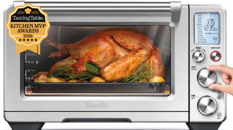 A close-up of a woman's hand adjusting the dial of a Breville Smart Oven Air Fryer Pro containing a whole roasted chicken