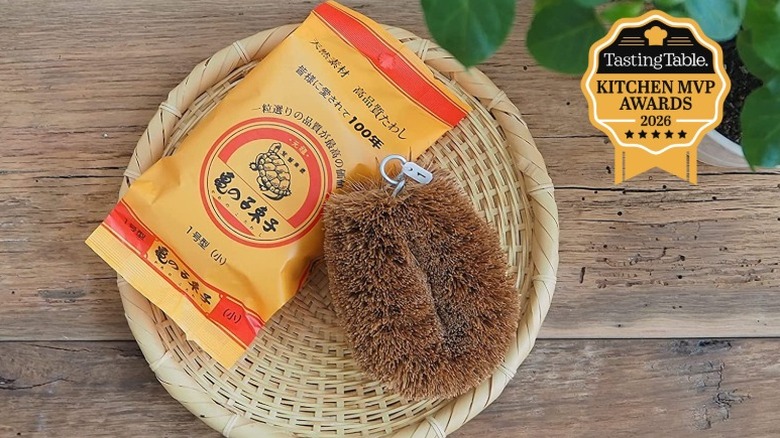 Kamenoko Tawashi scrub brush next to orange packaging with turtle logo on woven tray.