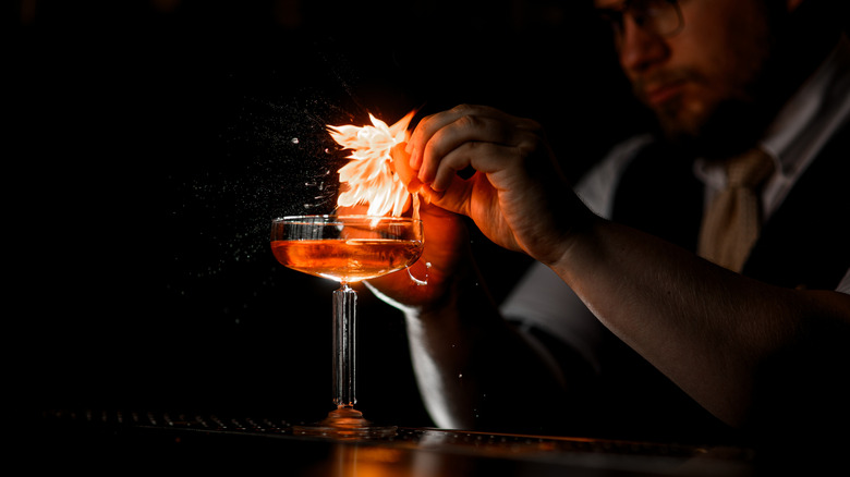 Bartender lights garnish over cocktail