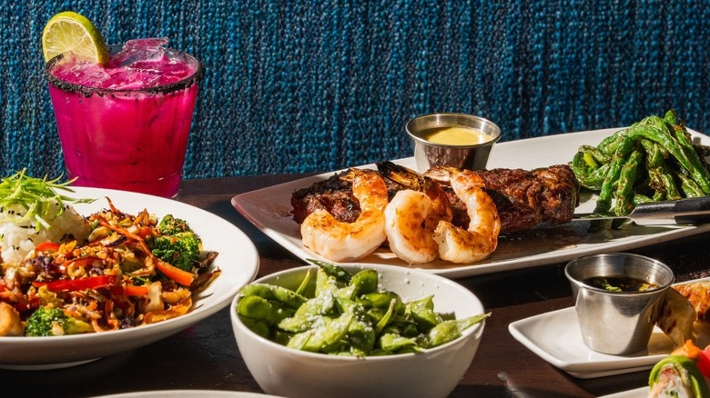 Kona Grill appetizers and entrées on a restaurant table with a cocktail