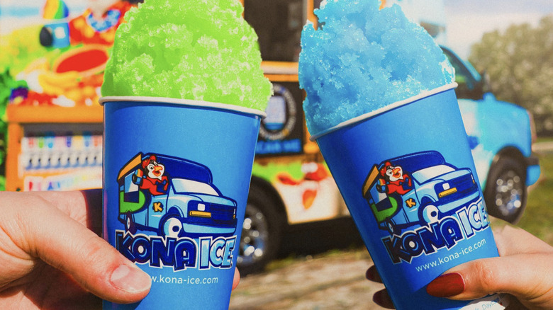 Two people holding up cups of shaved Kona Ice in front of the food truck