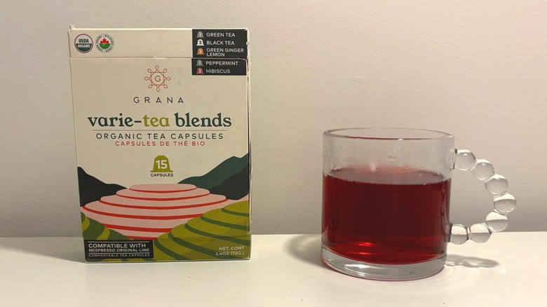 Box of Grana tea capsules next to clear mug of brewed tea on white background