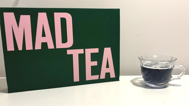Box of Mad Tea next to clear brewed cup on white background