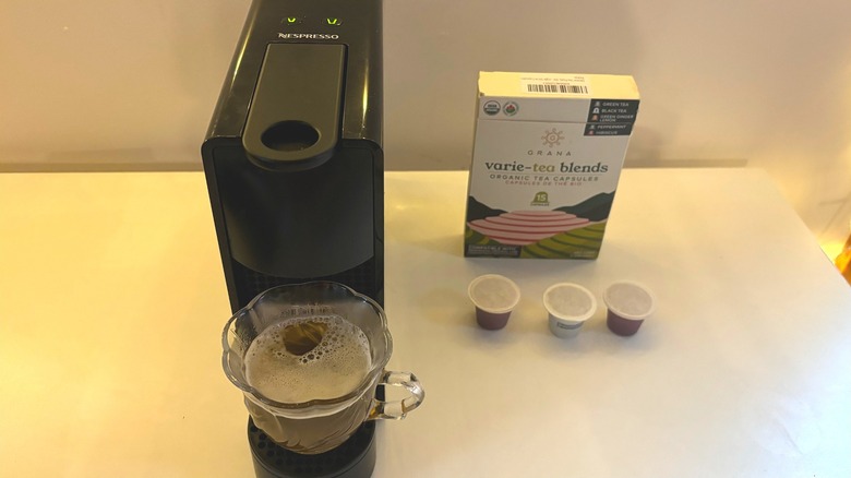 Nespresso machine brewing tea into clear teacup next to Grana tea pods