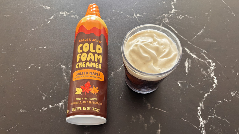 Trader Joe's salted maple cold foam creamer bottle next to cup of coffee with cold foam on top
