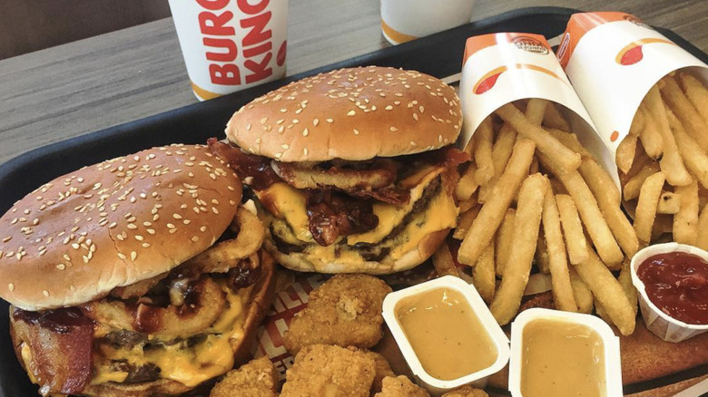 Two Burger King Rodeo Cheeseburger sit on a tray with fries and sauce.