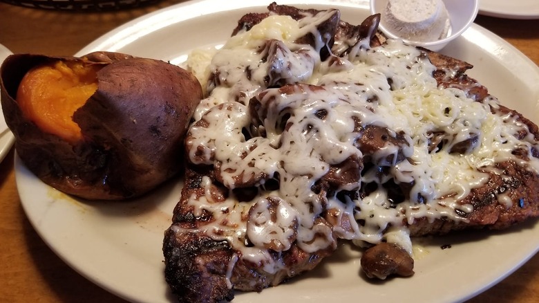 Texas Roadhouse porterhouse steak topped with mushrooms and jack cheese on white plate