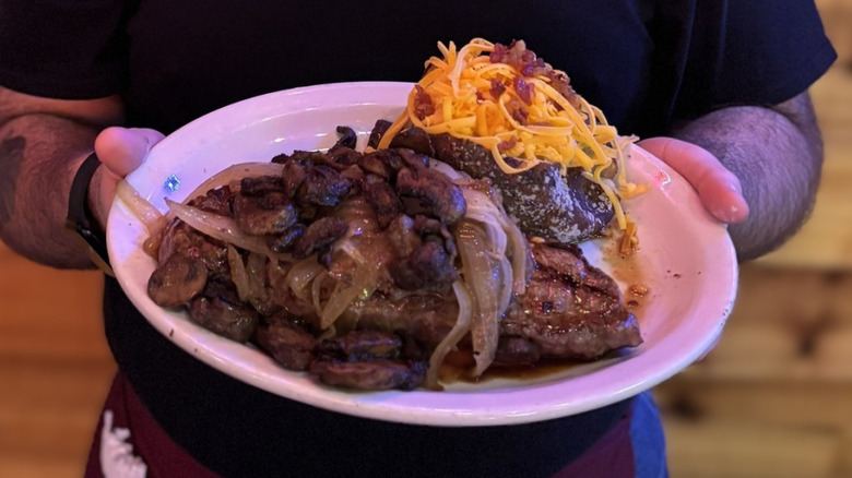 Texas Roadhouse server holding a plate with steak smothered with mushrooms and onions