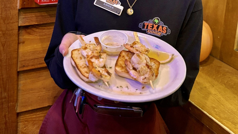 Texas Roadhouse server holding a plate with grilled shrimp sidekick