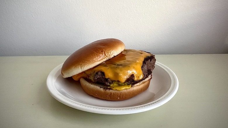 A plain cheeseburger on a white plate sits on a white table.