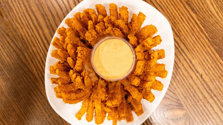 A fried onion blossom sits on a white plate on a wooden table