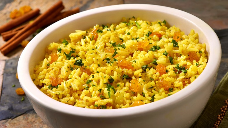 Yellow seasoned rice with onions and parsley in white bowl