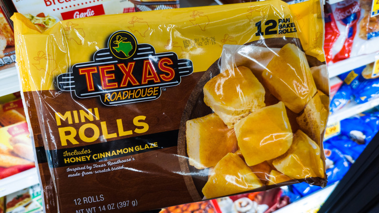 Texas Roadhouse mini rolls frozen package being held with other frozen breads blurring in the backgound