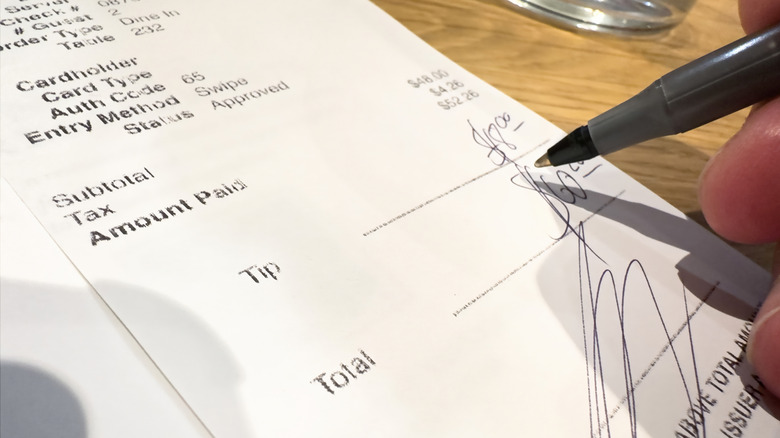 Someone holding a pen and feeling in the tip and total on a receipt