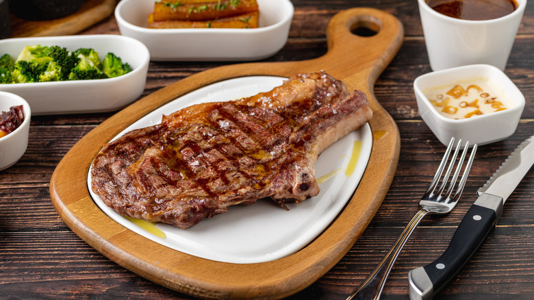 A large ribeye steak on a plate with sides, a fork, and a knife