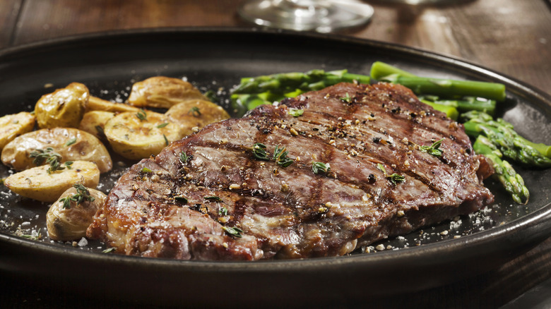 A cooked steak on a plate with roasted potatoes and asparagus.