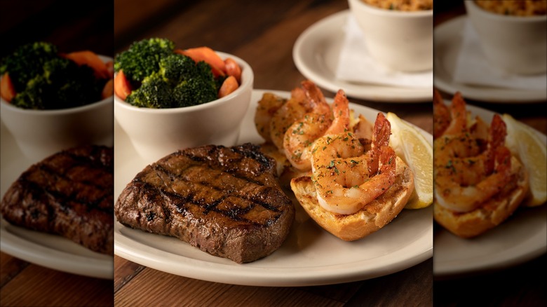 Texas Roadhouse sirloin steak on white place next to bowl of steamed vegetables and grilled shrimp on bread