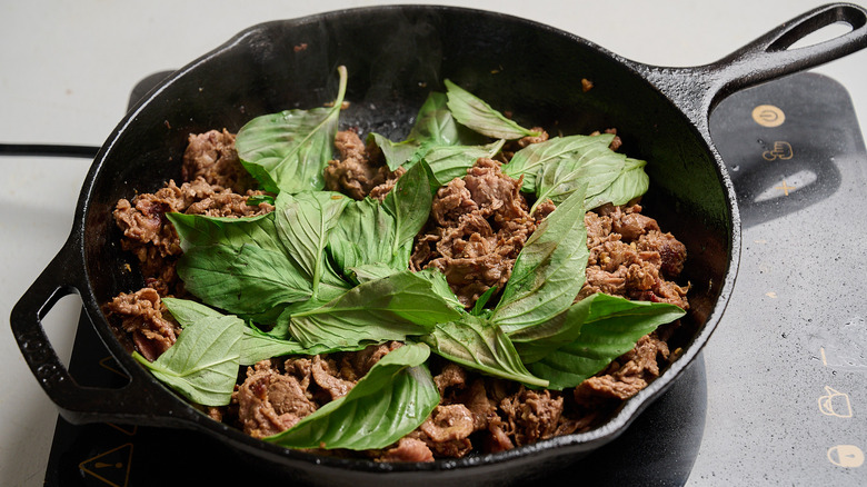 basil wilting onto beef in skillet