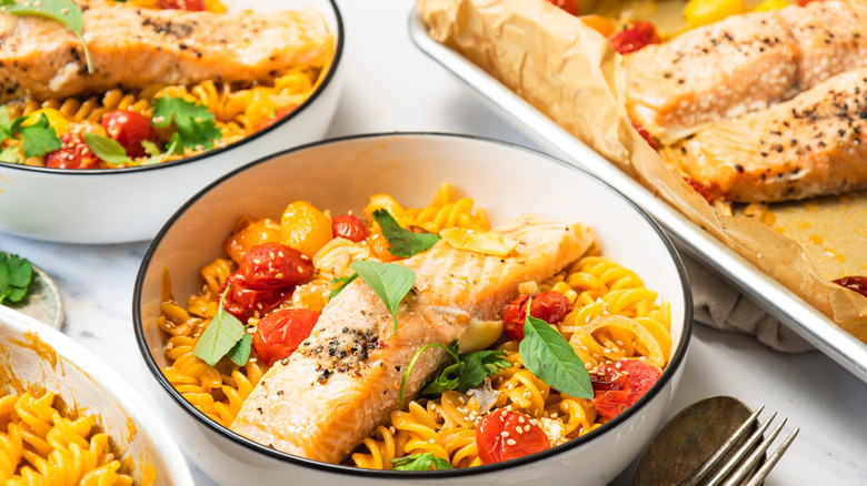 One bowl of Thai curry pasta with blistered tomatoes and salmon, and more in background.