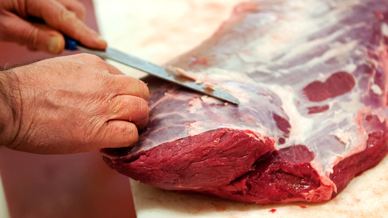 a butcher removing the silver skin off of a cut of beef