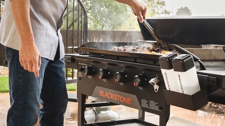 person cooking on a Blackstone griddle with a couple of accessories visible in a backyard