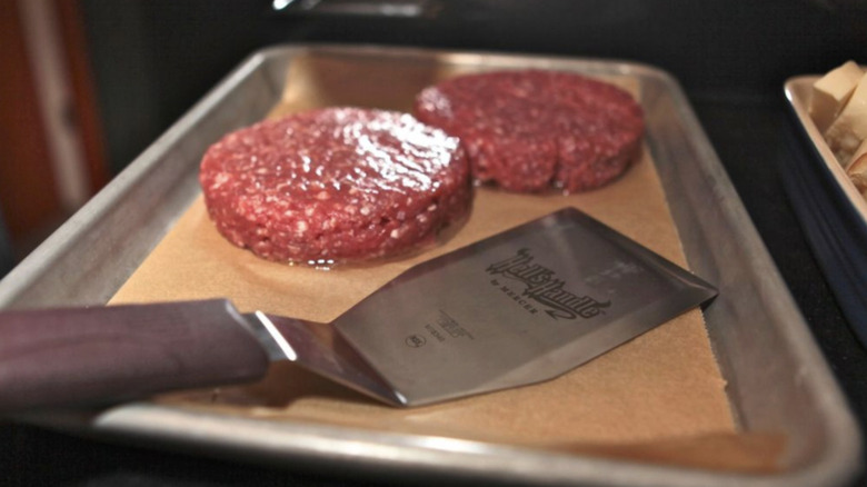 Turner grill spatula next to raw burger patties on a metal tray