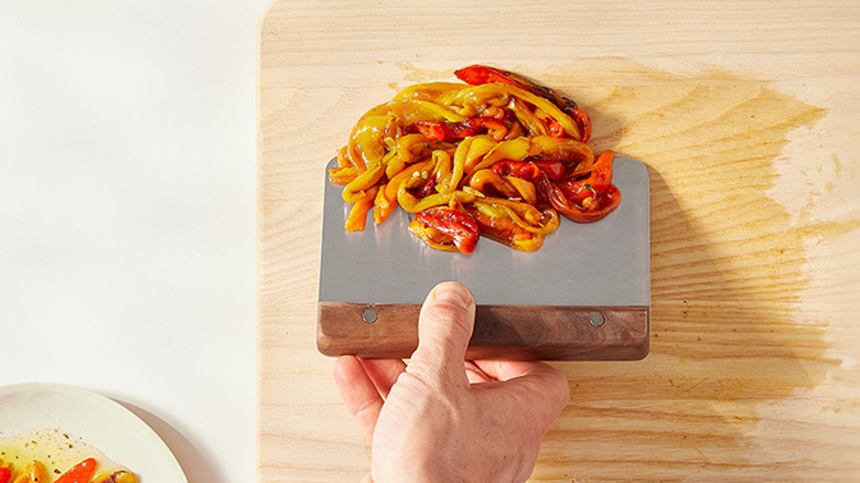 Stainless steel bench scraper with wood handle picking up peppers