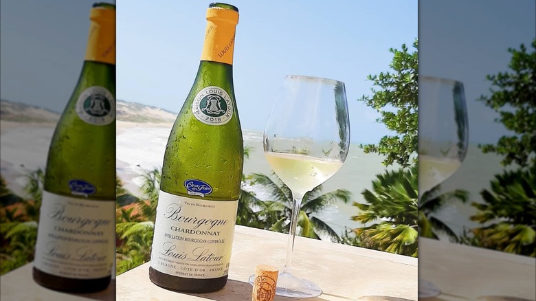 Louis Latour Chardonnay Bourgogne bottle and glass of white wine with palm trees and a beach in the background