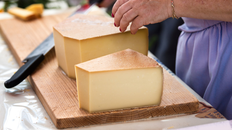 woman slicing a big round of Gruyère