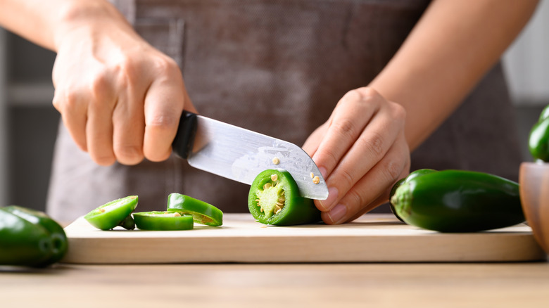 A chef putting a pepper on a generic cutting board with a large knife