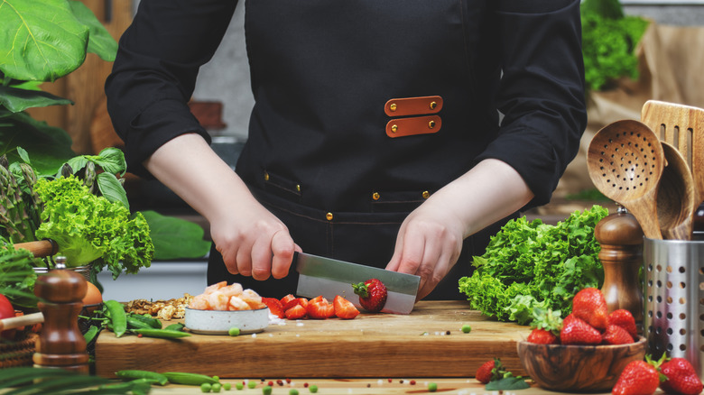 A chef chopping fruit on a cutting board surrounded by fresh ingredients