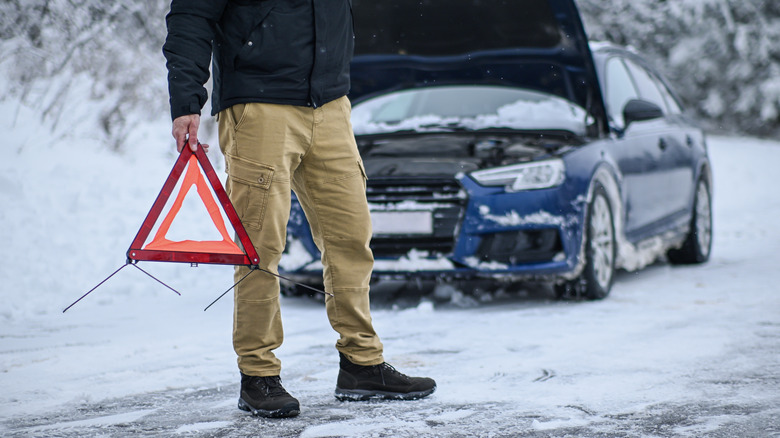Person holding visibility triangle in front of broken down car in winter