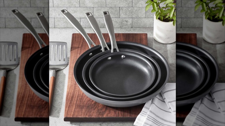Three Member's Mark hard anodized frying pans on a chopping board on a countertop