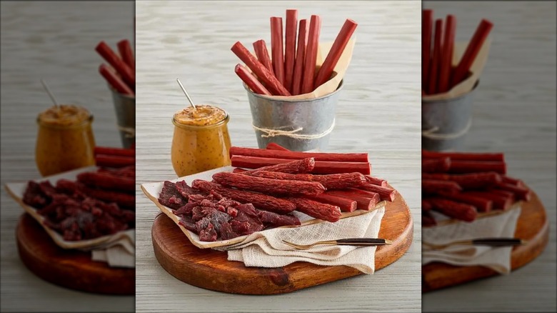 Various dried meat snacks from Harry & David on wooden board and inside tin cup next to jar of mustard