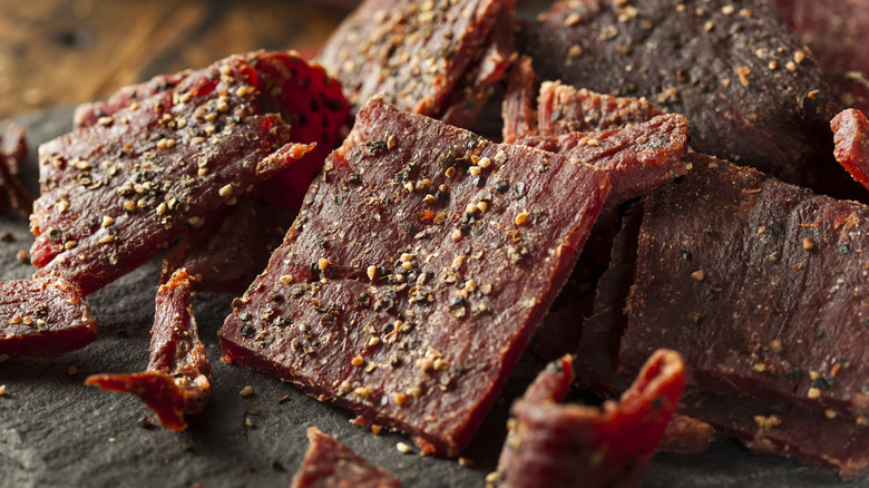 Square pieces of beef jerky with large grains of pepper on black surface