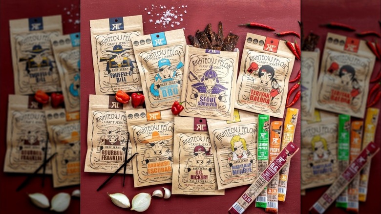 Paper bags of beef jerky and meat sticks from the Righteous Felon Beef Jerky & Meat Sticks Variety Pack on red surface