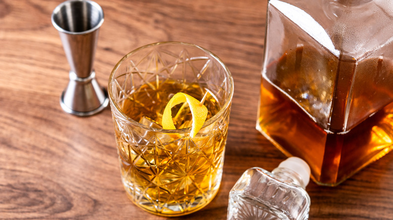 A bottle of bourbon next to an old fashioned cocktail in a tumbler