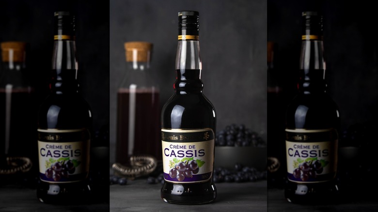A bottle of creme de cassis with blackcurrants in the background