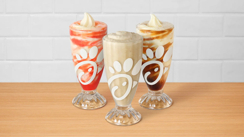 A trio of frosted sodas and floats from Chick-fil-A in parfait glasses on a wooden table