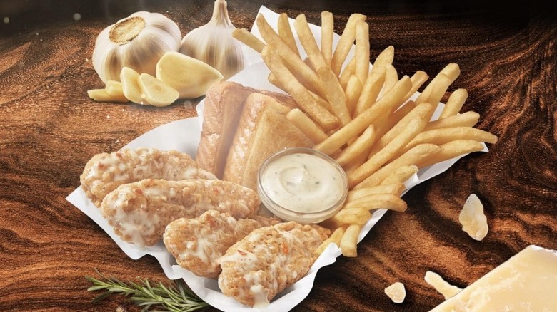A basket of parmesan garlic chicken strips with dip, french fries, and toast on a wooden table