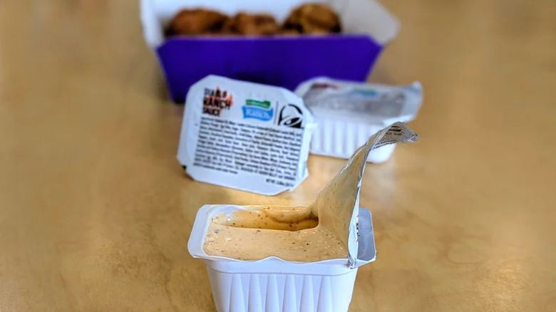 An open packet of creamy orange sauce with chicken nuggets in the background