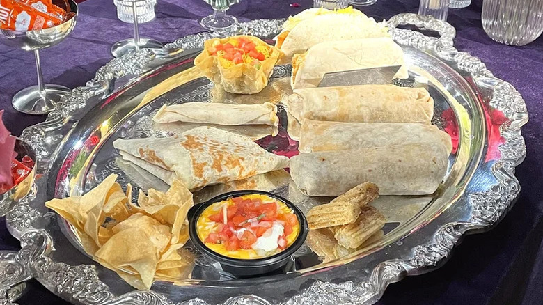 A silver serving platter adorned with burritos, churros, nachos, and other taco bell food items