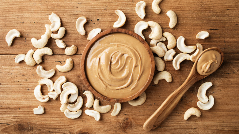 Cashew butter in wooden bowl next to spoon and cashew nuts
