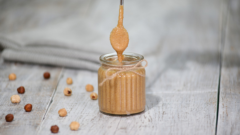 Hazelnut butter dripping from spoon into glass jar