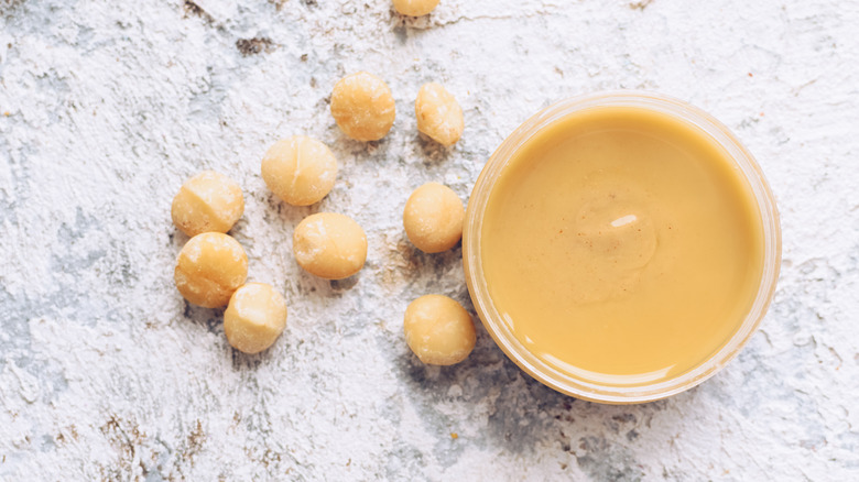 Top down view of macadamia nut butter in glass jar, next to whole macadamia nuts