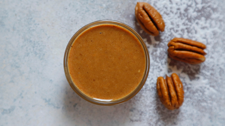 Top down view of pecan butter in glass jar, next to whole pecans